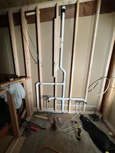 Plumbing installation with exposed pipes and tools in a framed wall setting.