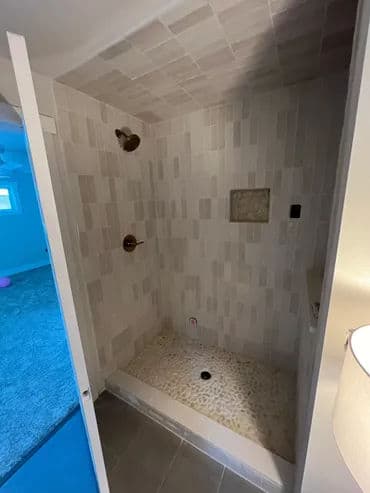 Modern walk-in shower with stone floor and dual showerheads in tiled bathroom.